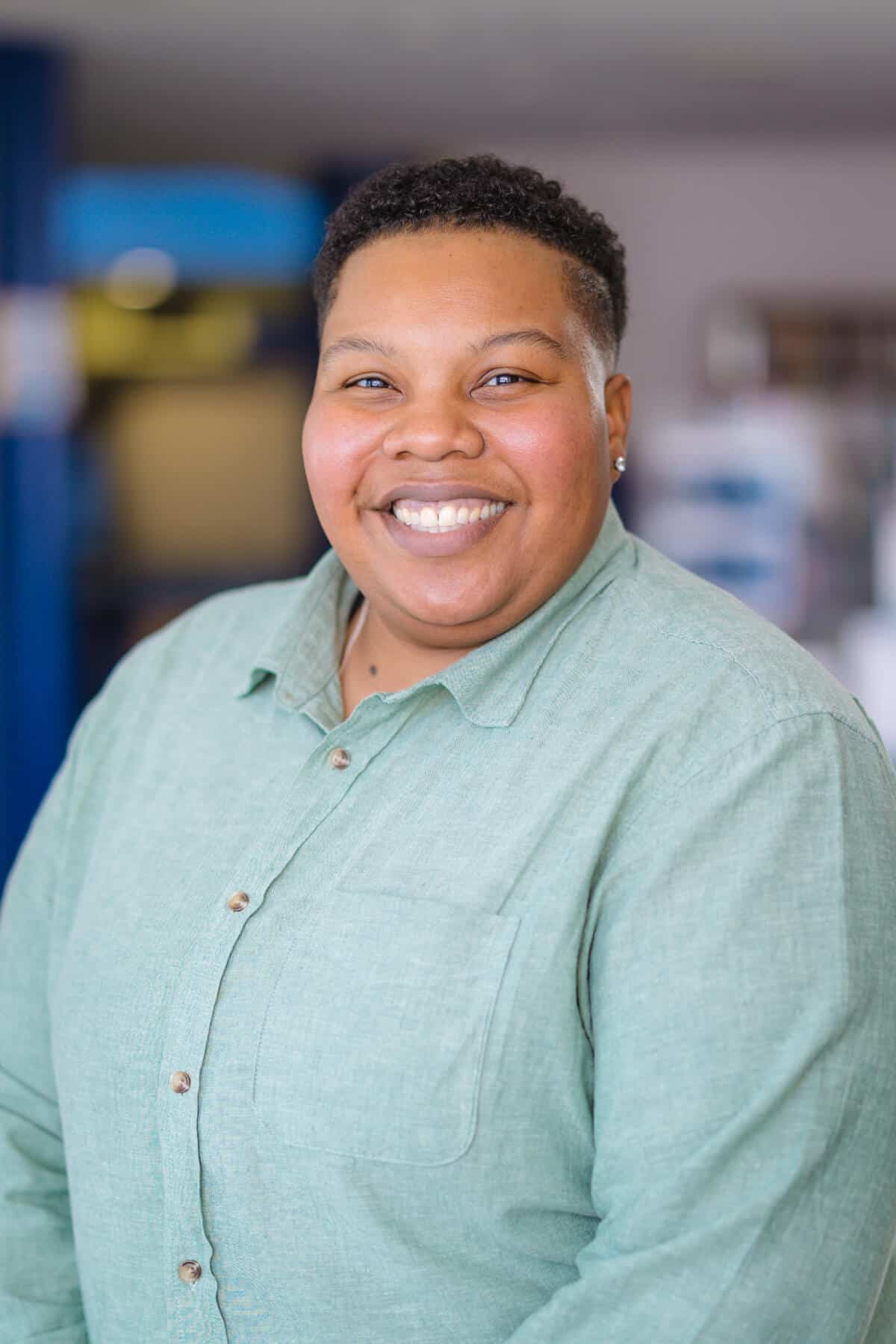 Headshot of a black woman with short hair wearing a green button-up shirt