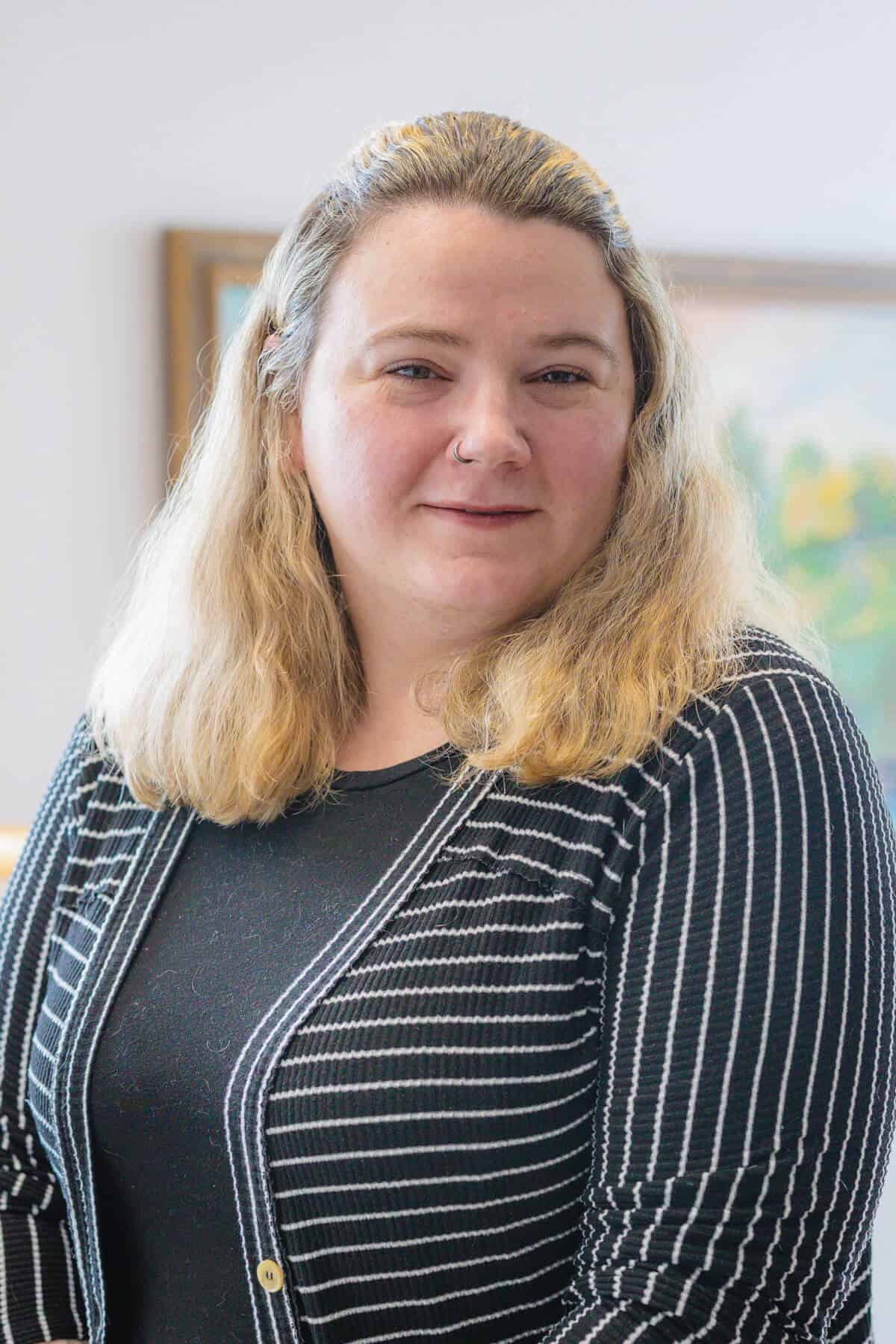 Headshot of a white woman with blond hair wearing a striped black and white suit jacket