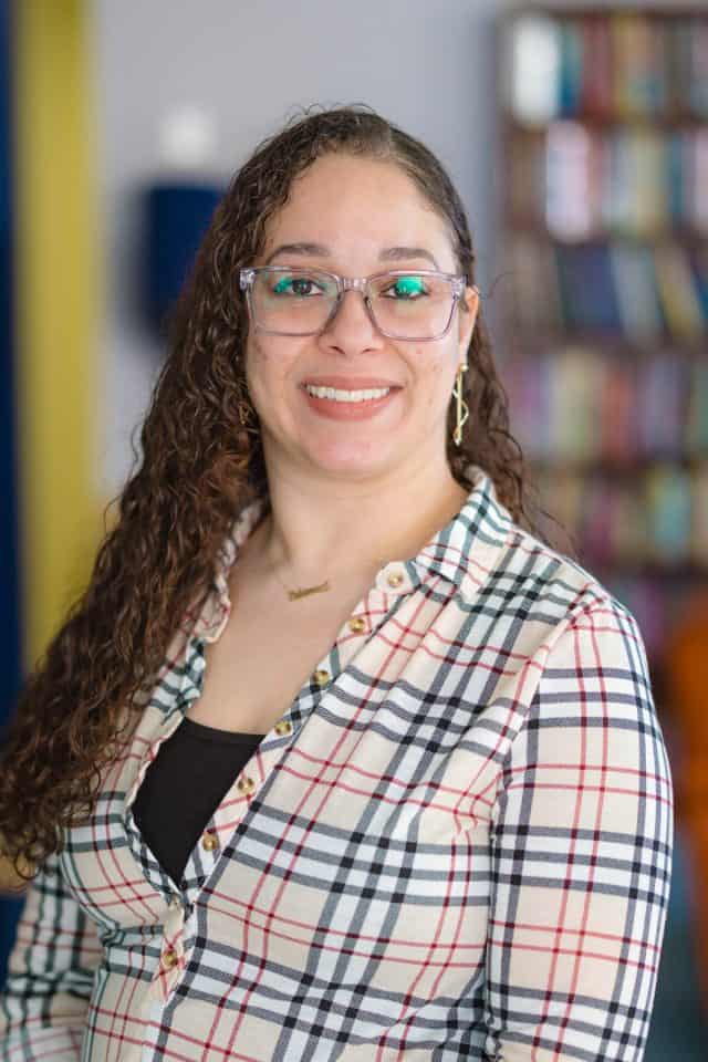 Woman with long hair wearing a striped button-up shirt and glasses smiling